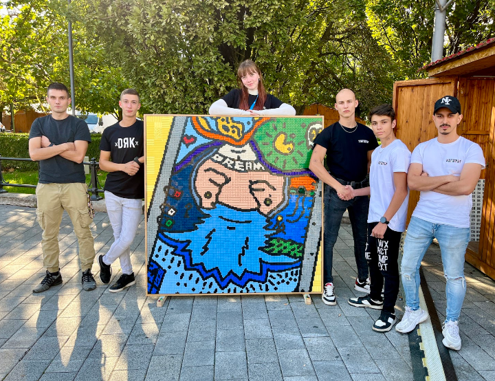 Group of people standing outdoors with a colorful painting of a cartoon character. LEGO